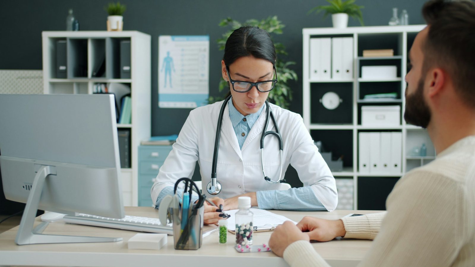 Médica escreve em documentos enquanto conversa com um paciente durante uma consulta no consultório
