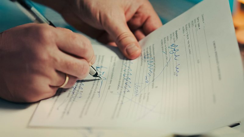 Mãos assinando um documento com caneta sobre a mesa
